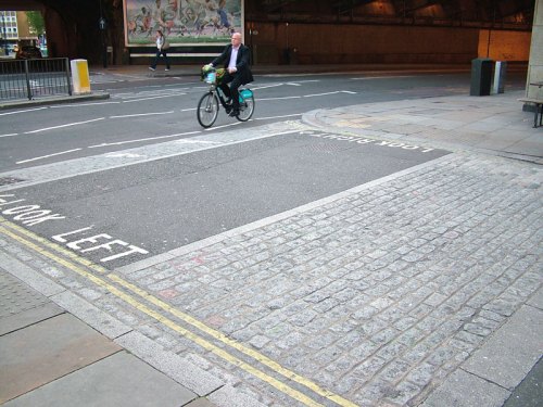 A British attempt at a continuous-path junction, which fails as the path is still clearly severed by the road, even though it rises up, the double yellow lines continue around the junction, and "look left" and "look right" are painted on the floor next to tactile paving.