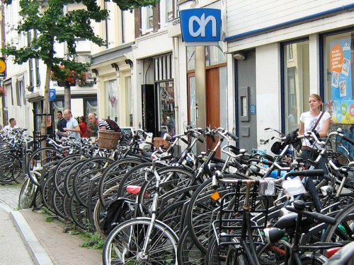 A huge number of bikes parked outside a supermarket in Utrecht, Netherlands. Shoppers can be seen.
