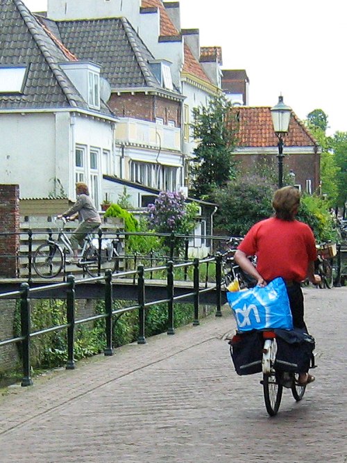 A person cycles home from the shops in Amersfoort, Netherlands. Both panniers are full and they are holding a large shopping bag on the rack behind them.