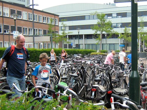 A bike parking lot outside a supermarket in the Netherlands. Hundreds of bikes can be seen with customers amongst them.