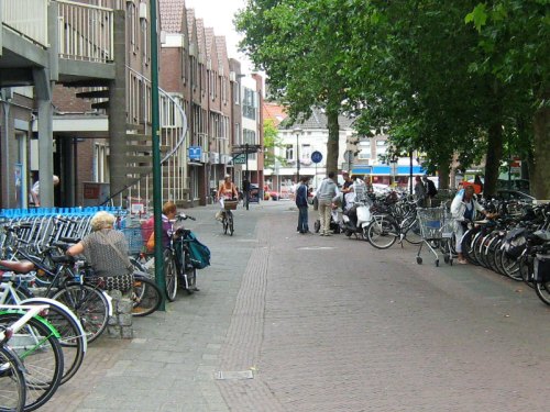 Bikes parked outside a supermarket in Woerden, Netherlands. Shoppers are loading items into their bikes' panniers. The bike parking is nearer to the shop entrance than the car parking!